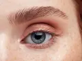 Nahaufnahme eines blauen Auges mit Sommersprossen und perfekt geformten Augenbrauen.