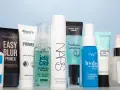 Eine Reihe von Make-up-Primern in verschiedenen Größen und Marken, auf hellblauem Hintergrund.