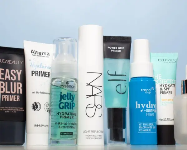 Eine Reihe von Make-up-Primern in verschiedenen Größen und Marken, auf hellblauem Hintergrund.
