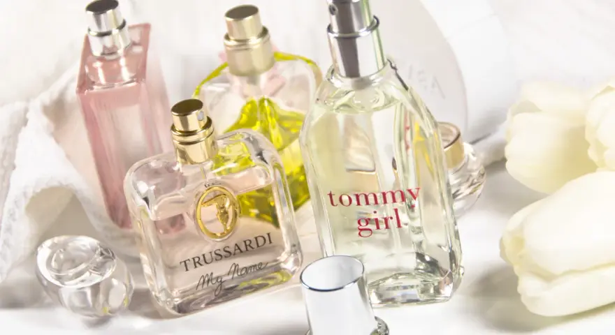 Mehrere Parfümflaschen, darunter Trussardi und Tommy Girl, auf weißem Handtuch mit weißen Tulpen.
