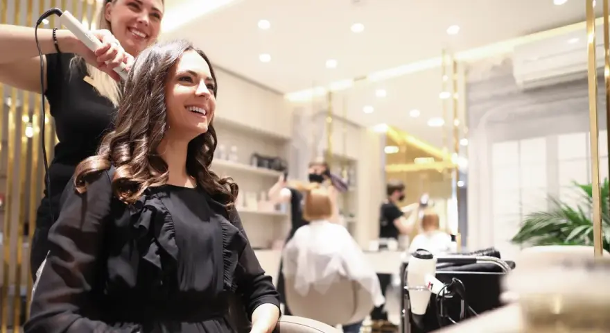 Friseurin stylt lächelnde Kundin mit Lockenstab in modernem Salon.