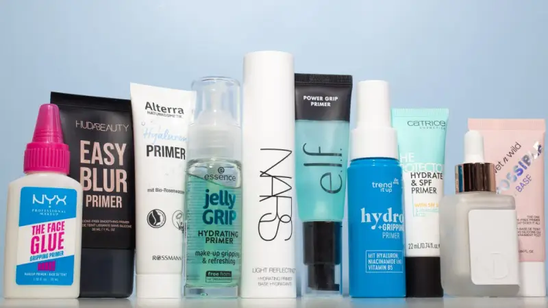Eine Reihe von Make-up-Primern in verschiedenen Größen und Marken, auf hellblauem Hintergrund.